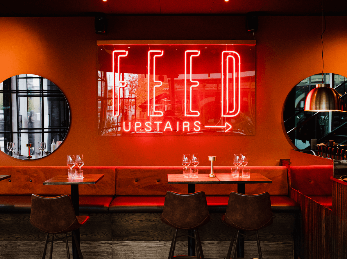 Billede af et neonskilt fra Feed Bistro med teksten 'Feed Upstairs''